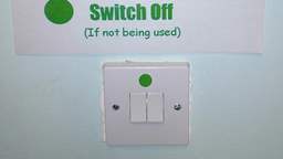 Green dot on light switch denoting switch off if not being used