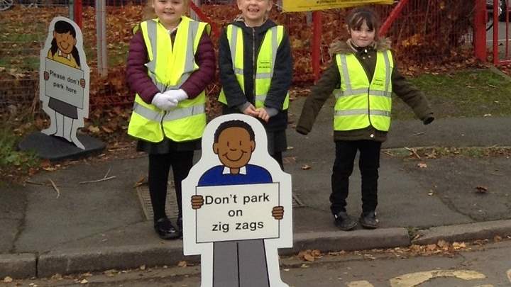 Three children outside Trinity Primary School with a don't park on zig zags sign