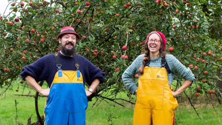 Tom and Lydia from Artistraw Cider standing in front of some apple trees. Photo credit Billie Charity