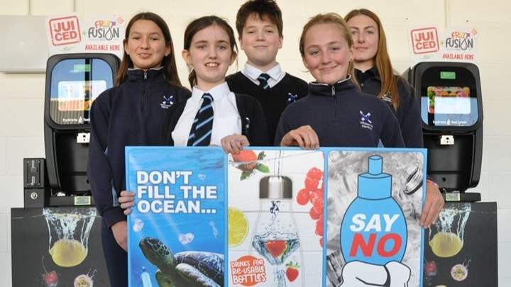 A group of 5 students stand behind a banner of images and text discouraging plastic use and encouraging re-usable bottles