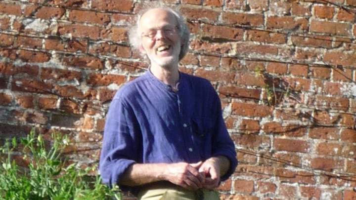 Man in purple shirt smiles at camera on a bright day in a walled garden